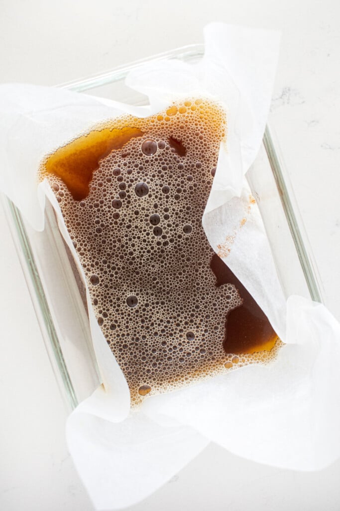 brown butter in a tupperware with parchment paper on a marble counter.