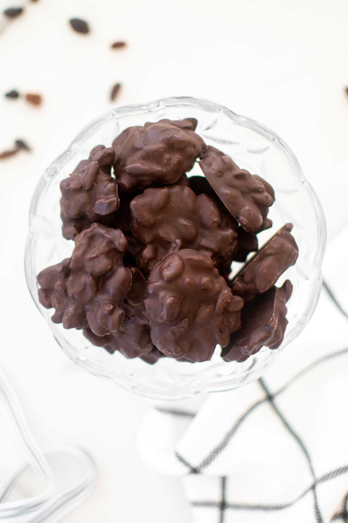 chocolate covered raisin clusters in a glass dish on a white marble counter.