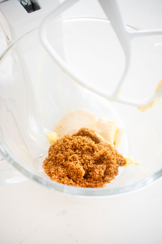 butter and sugar in a glass mixing bowl on a marble counter.
