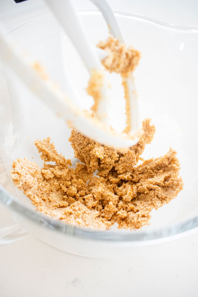 creamed butter and sugar in a glass mixing bowl on a white marble counter.