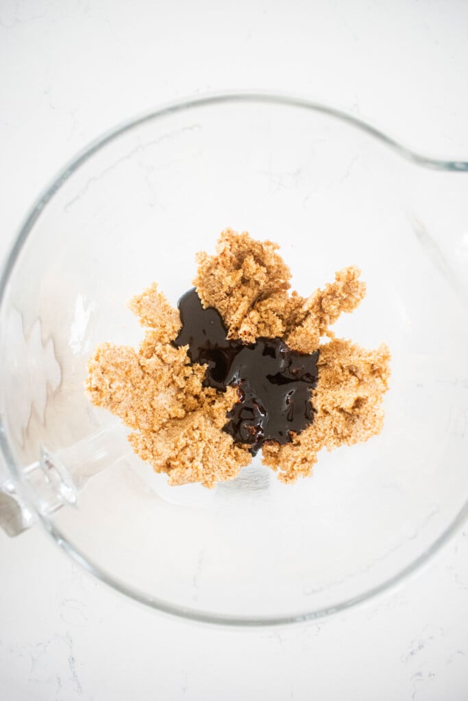 creamed butter and sugar in a glass mixing bowl with molasses on a white marble counter.
