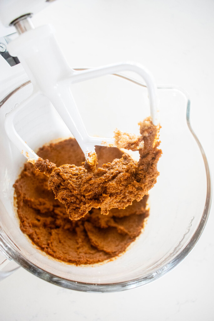 creamed butter sugar and molasses in a glass mixing bowl on a white marble counter.
