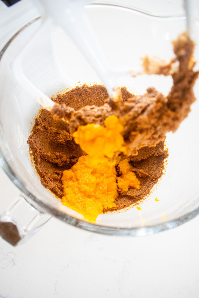 creamed butter sugar and molasses with pumpkin in a glass mixing bowl on a white marble counter.