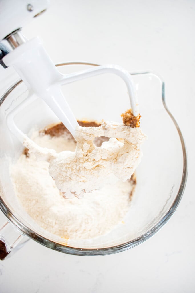 ingredients for eggless pumpkin gingerbread cookies in a glass mixing bowl on a white marble counter.