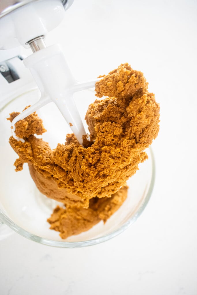 eggless pumpkin gingerbread cookie dough in a glass mixing bowl on a white marble counter.