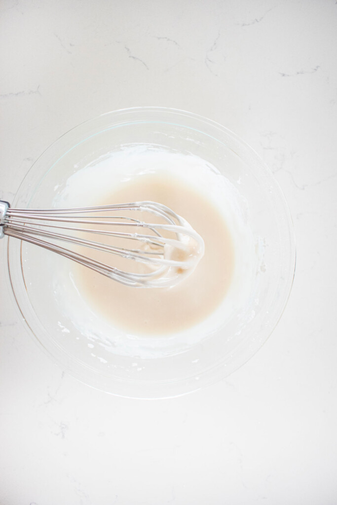 glaze in a glass mixing bowl with a whisk on a white marble counter.
