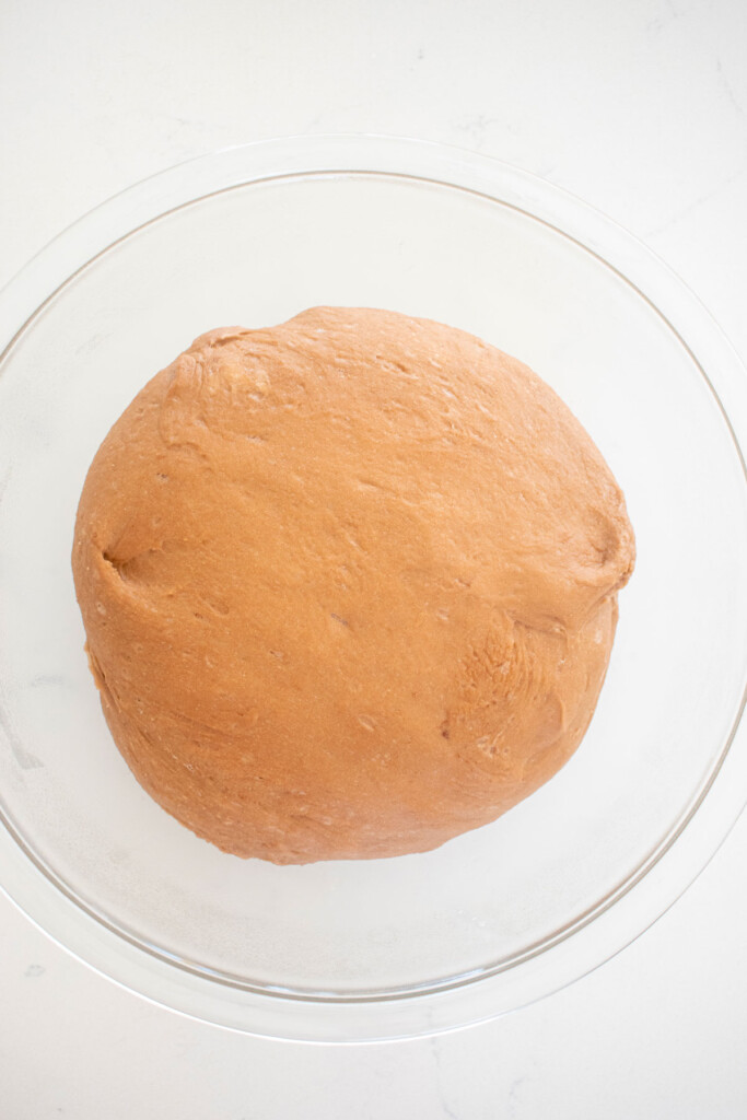 hot chocolate sweet roll dough in a glass mixing bowl on a white marble counter.