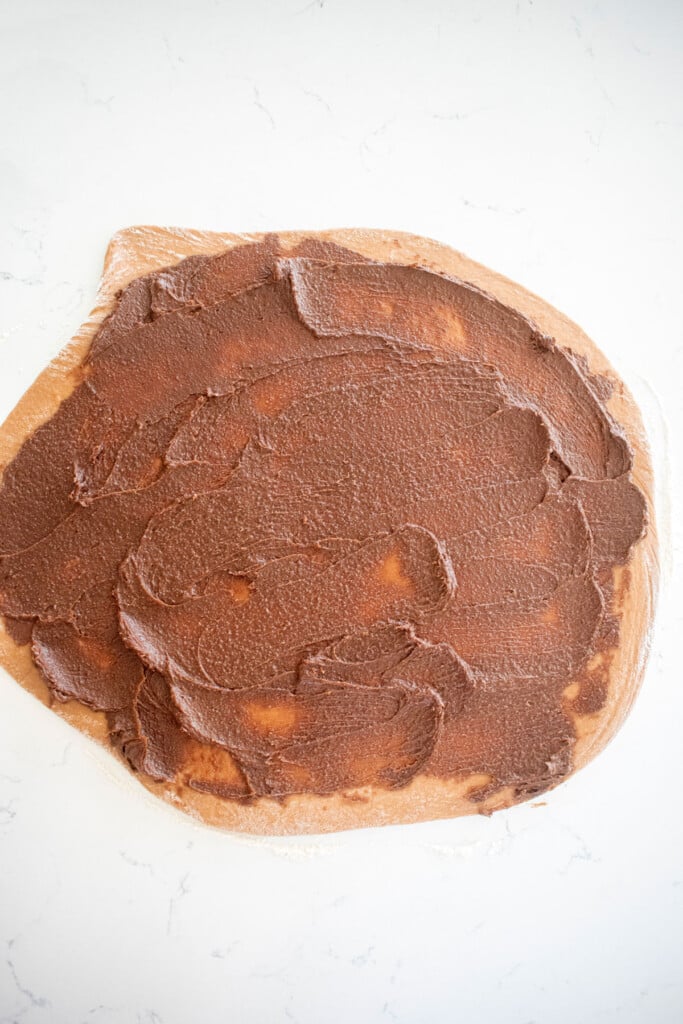 hot chocolate sweet roll dough with hot chocolate filling spread onto it on a white marble counter.