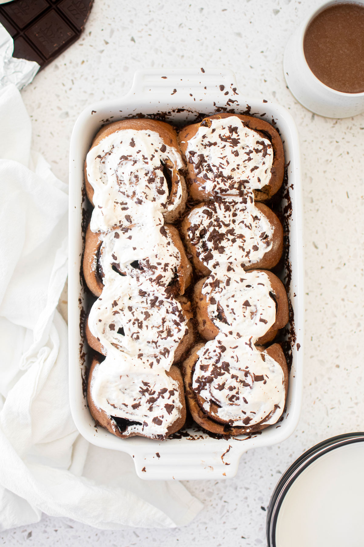 hot chocolate sweet rolls with marshmallow topping and shaved chocolate in a white baking dish on a white marble counter.