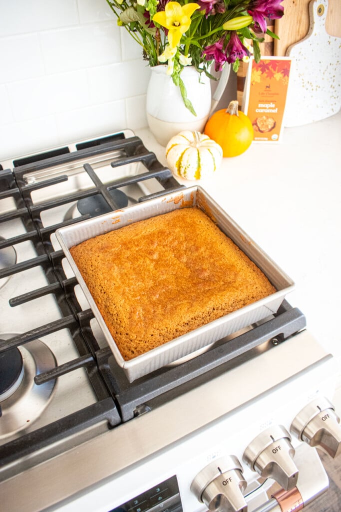 baked maple spice cake in a square cake pan cooling on top of an oven.