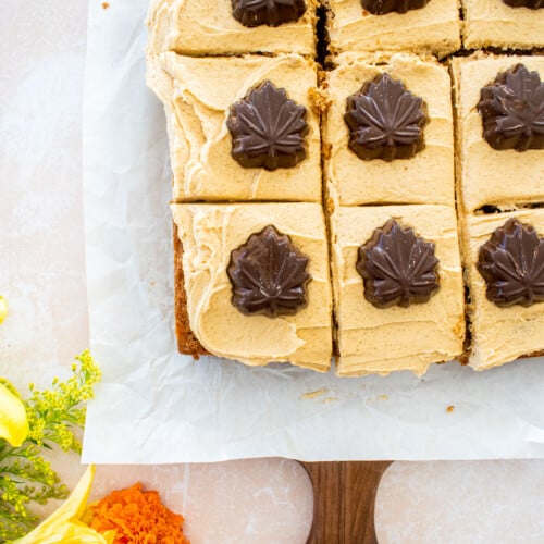 maple spice cake with brown sugar frosting and chocolate maple leaves cut into squares on a table with fresh flowers.