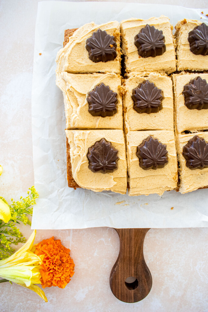 maple spice cake with brown sugar frosting and chocolate maple leaves cut into squares on a table with fresh flowers.
