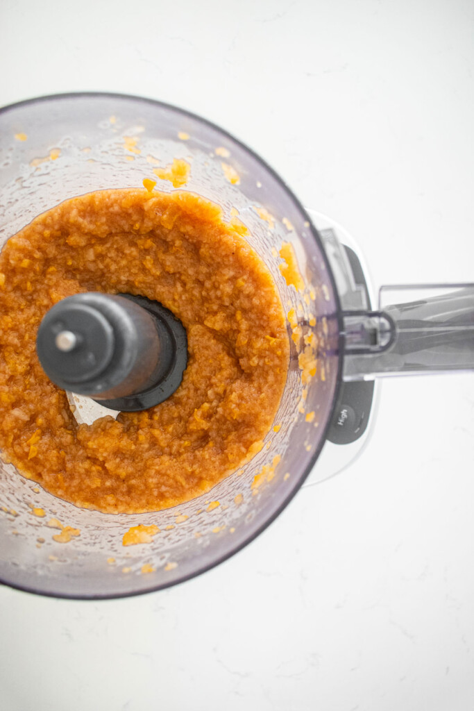persimmon apple cider jam in a food processor on a white marble counter.