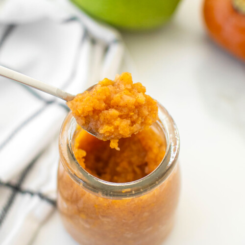 persimmon apple cider jam in a glass jar on a white marble counter.