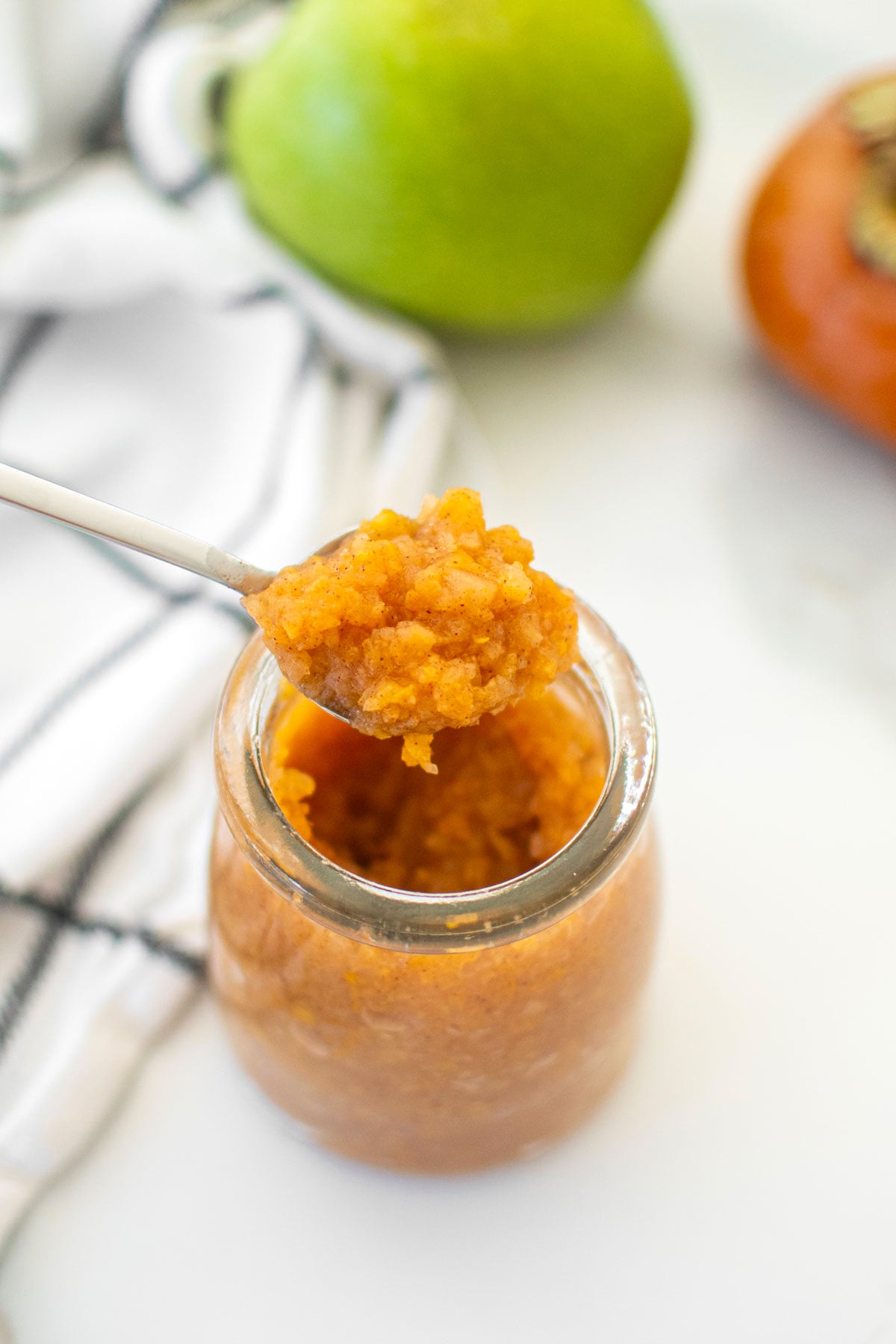 persimmon apple cider jam in a glass jar on a white marble counter.