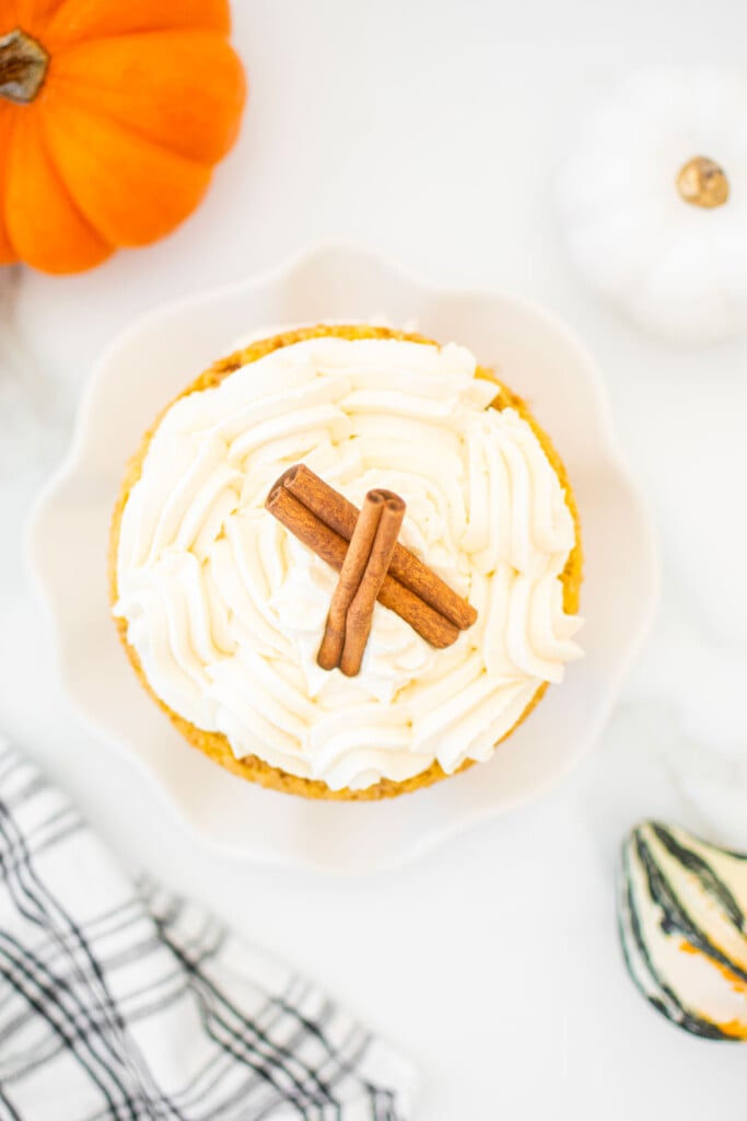 top of pumpkin pie layer cake with cinnamon sticks on a ruffle cake plate on a marble kitchen countertop.