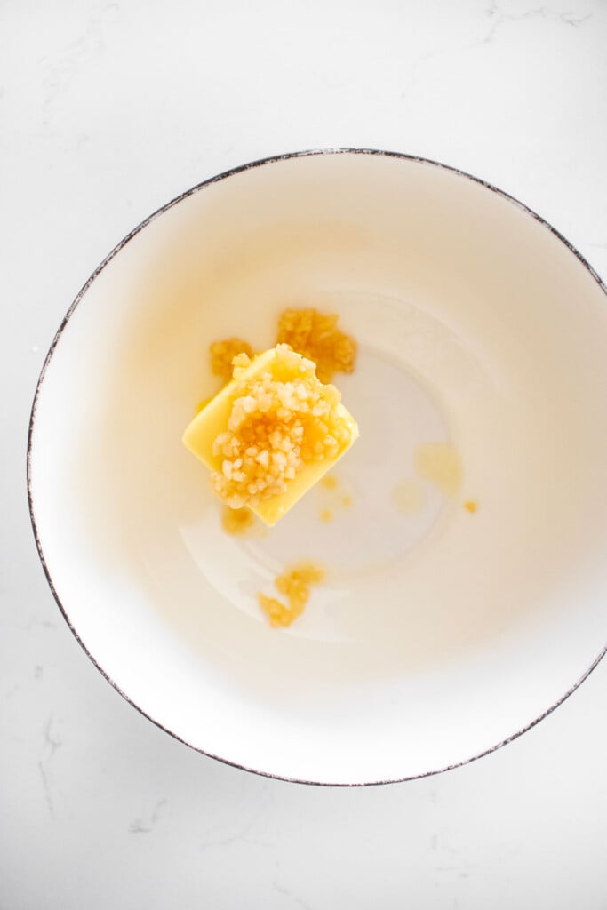 butter and garlic in a bowl on a white marble counter.