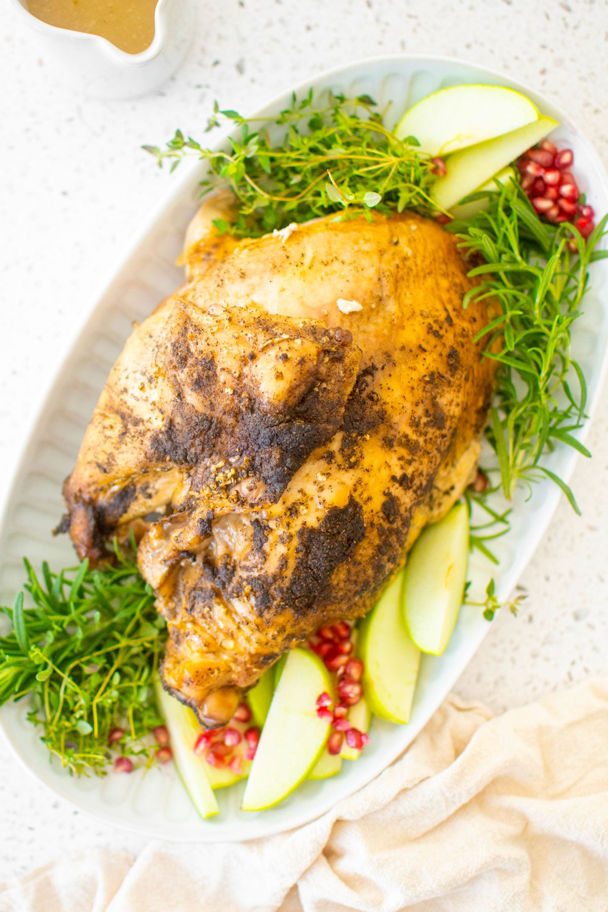 slow cooker turkey on a platter with rosemary apples and pomegranates on a white marble table.