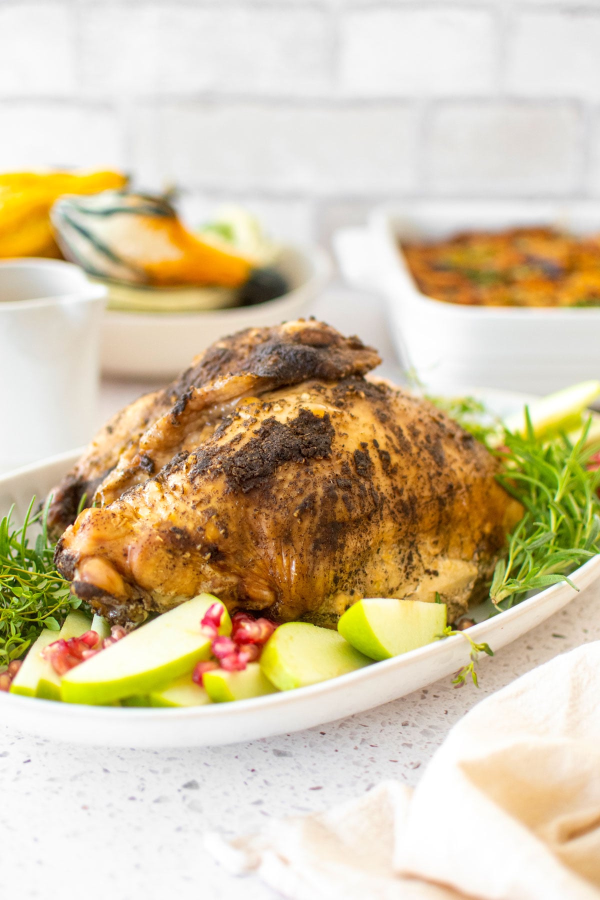 slow cooker turkey on a platter with rosemary apples and pomegranates on a white marble table with thanksgiving sides.