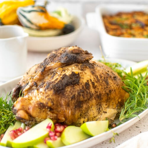 slow cooker turkey on a platter with rosemary apples and pomegranates on a white marble table with thanksgiving sides.