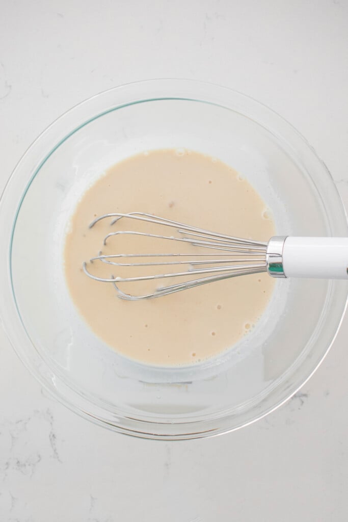 sourdough discard and yeast being whisked into a glass mixing bowl on a marble counter.