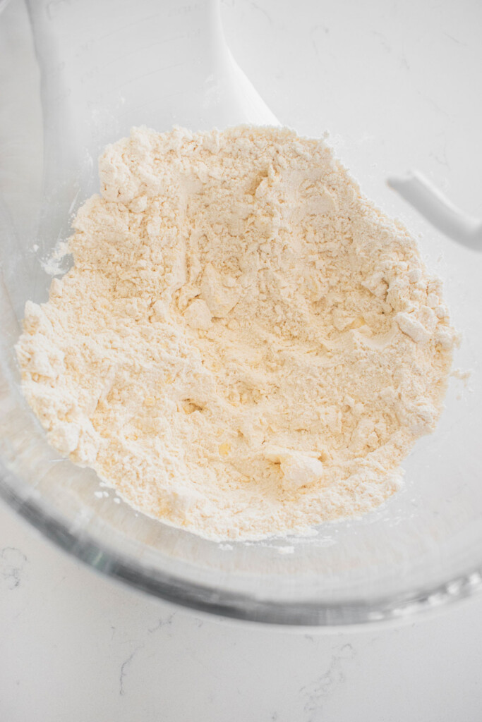 ingredients for sourdough crescent roll dough in a glass mixing bowl on a white marble counter.