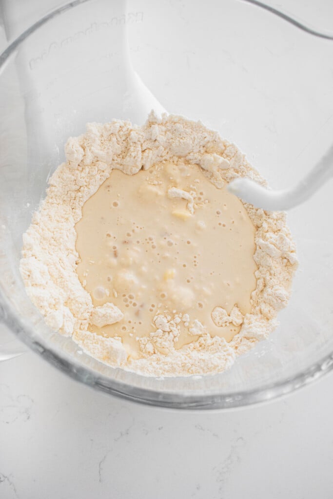 ingredients for sourdough crescent roll dough in a glass mixing bowl on a white marble counter.