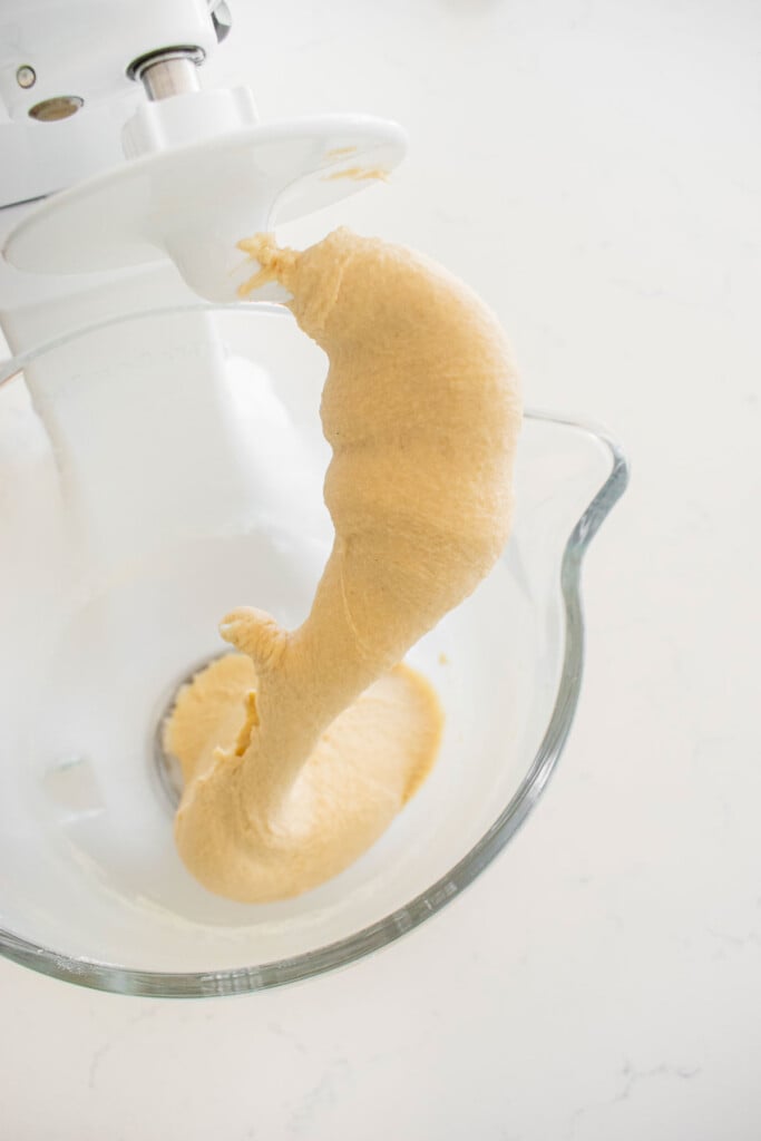 sourdough crescent roll dough in a glass mixing bowl on a white marble counter.