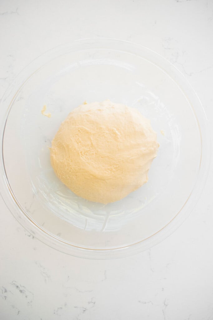 sourdough crescent roll dough in a glass mixing bowl on a white marble counter.