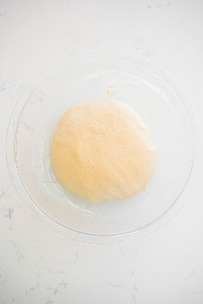 sourdough crescent roll dough in a glass mixing bowl on a white marble counter.