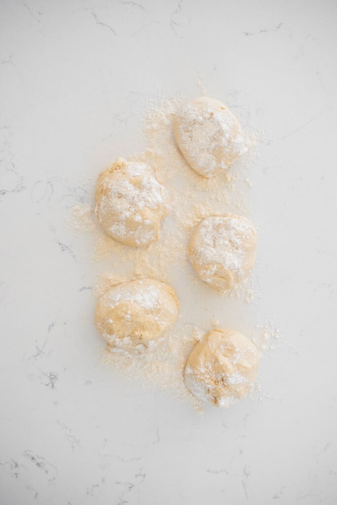 sourdough crescent roll dough balls sprinkled with flour on a marble counter.