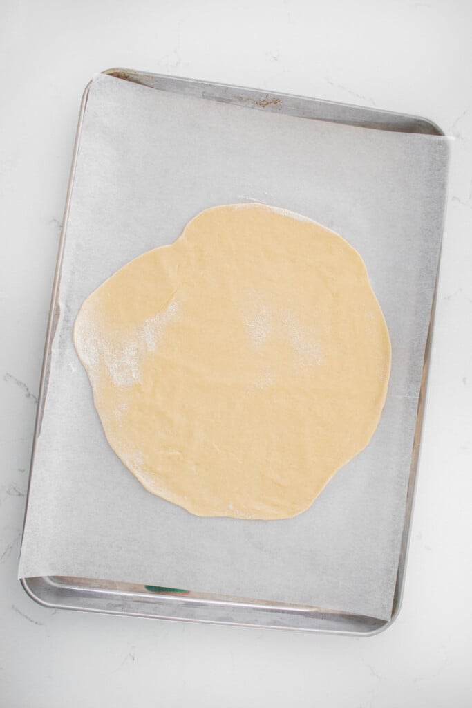 sourdough crescent roll dough on a baking sheet on a marble counter.