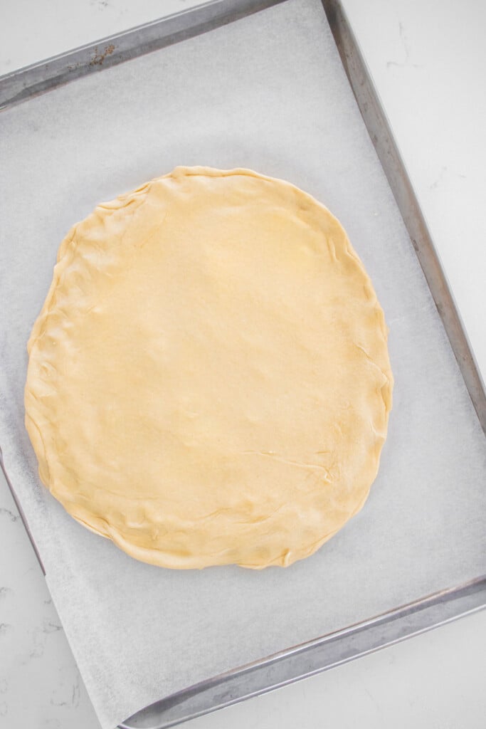 sourdough crescent roll dough on a baking sheet on a marble counter.