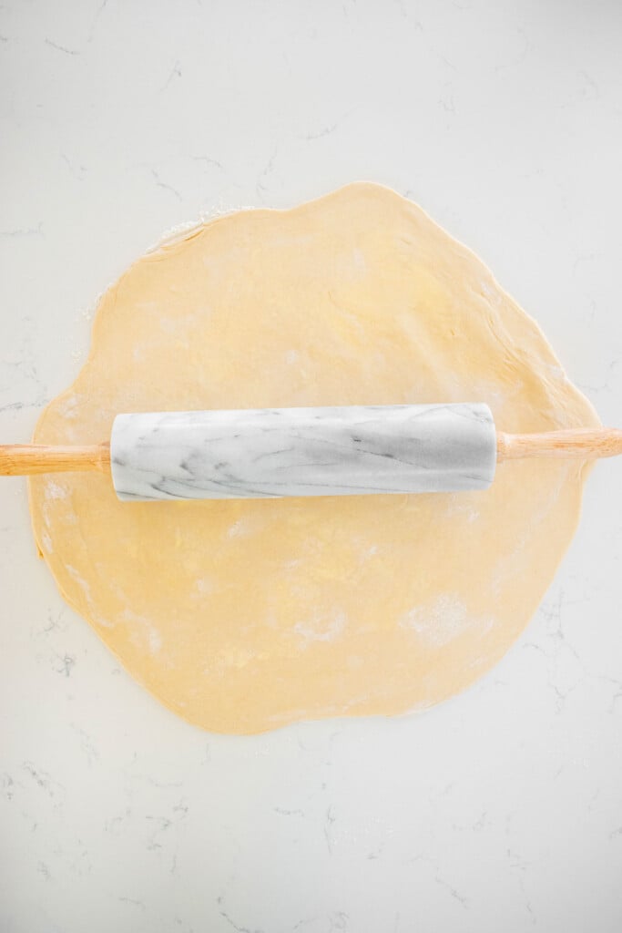 sourdough crescent roll dough being rolled out on a marble counter.