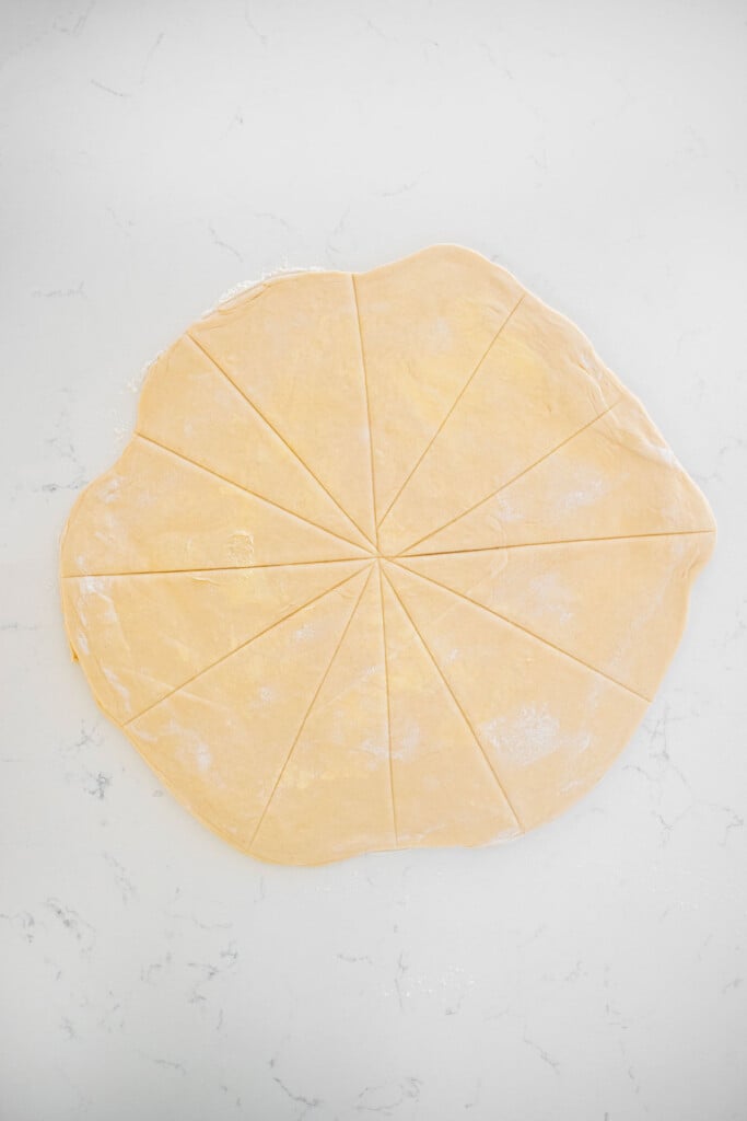 sourdough crescent rolls dough cut into triangles on a white marble counter.