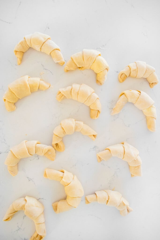 sourdough crescent rolls rolled into the crescent shape on a white marble counter.