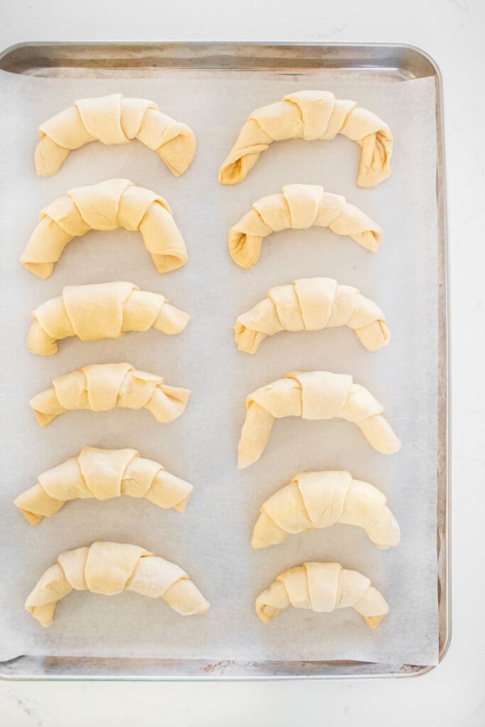 sourdough crescent rolls on a baking sheet on a marble counter.