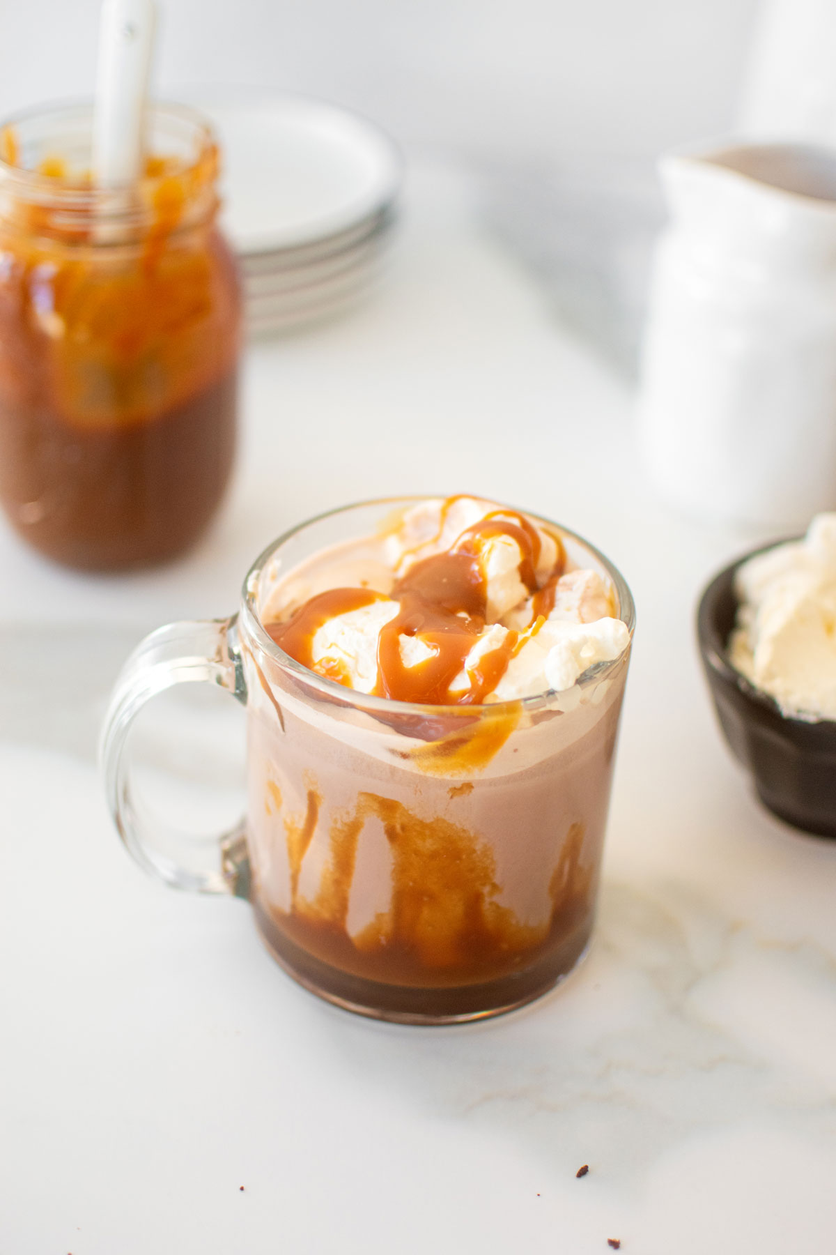 caramel hot cocoa with whipped cream and caramel sauce on a white marble counter.