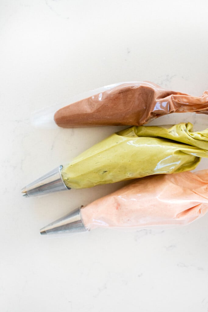frosting bags of chocolate, green and link pink on a marble counter.