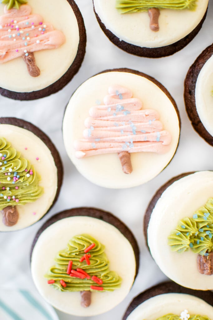 chocolate peppermint christmas tree cupcakes on a marble counter with different buttercream trees on each one.