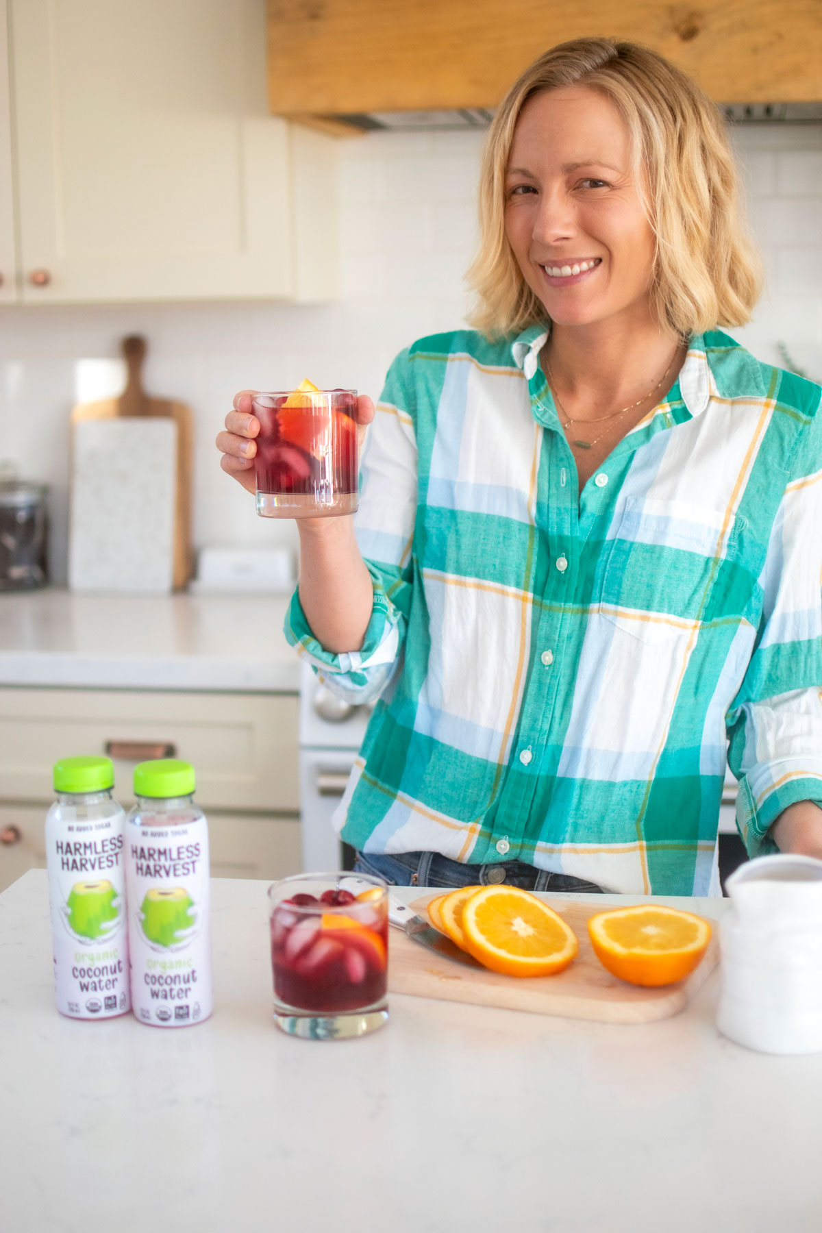 woman holding a cranberry mocktail with coconut water at the kitchen counter.