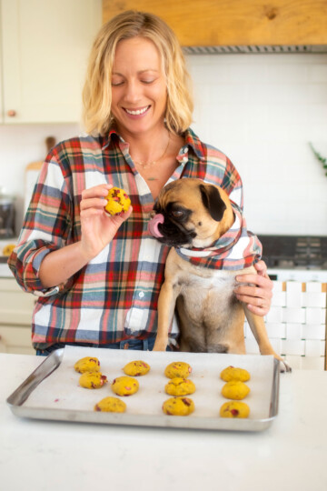 woman and pug in the kitchen eating cranberry pumpkin dog cookies at the counter.