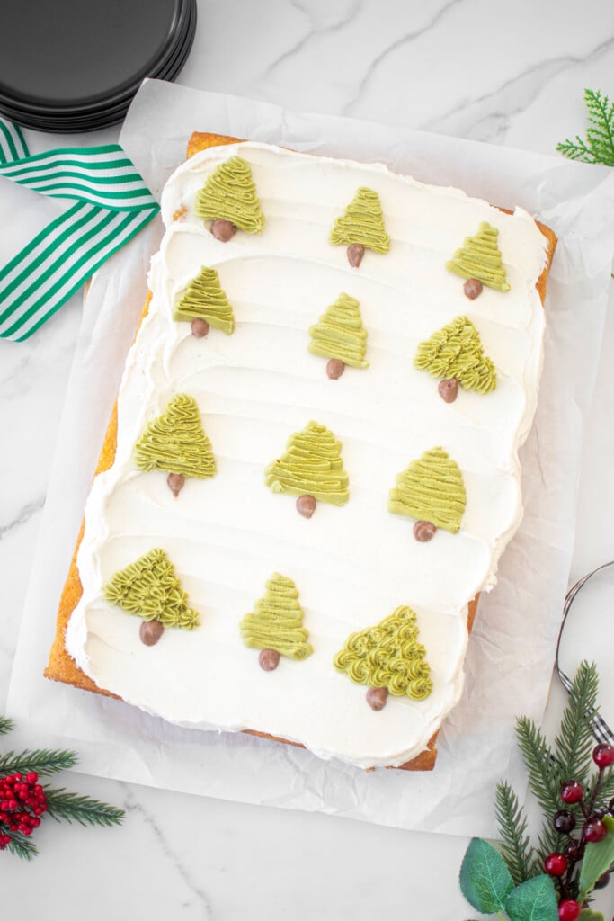eggnog sheet cake with buttercream christmas trees piped onto it on a marble counter.