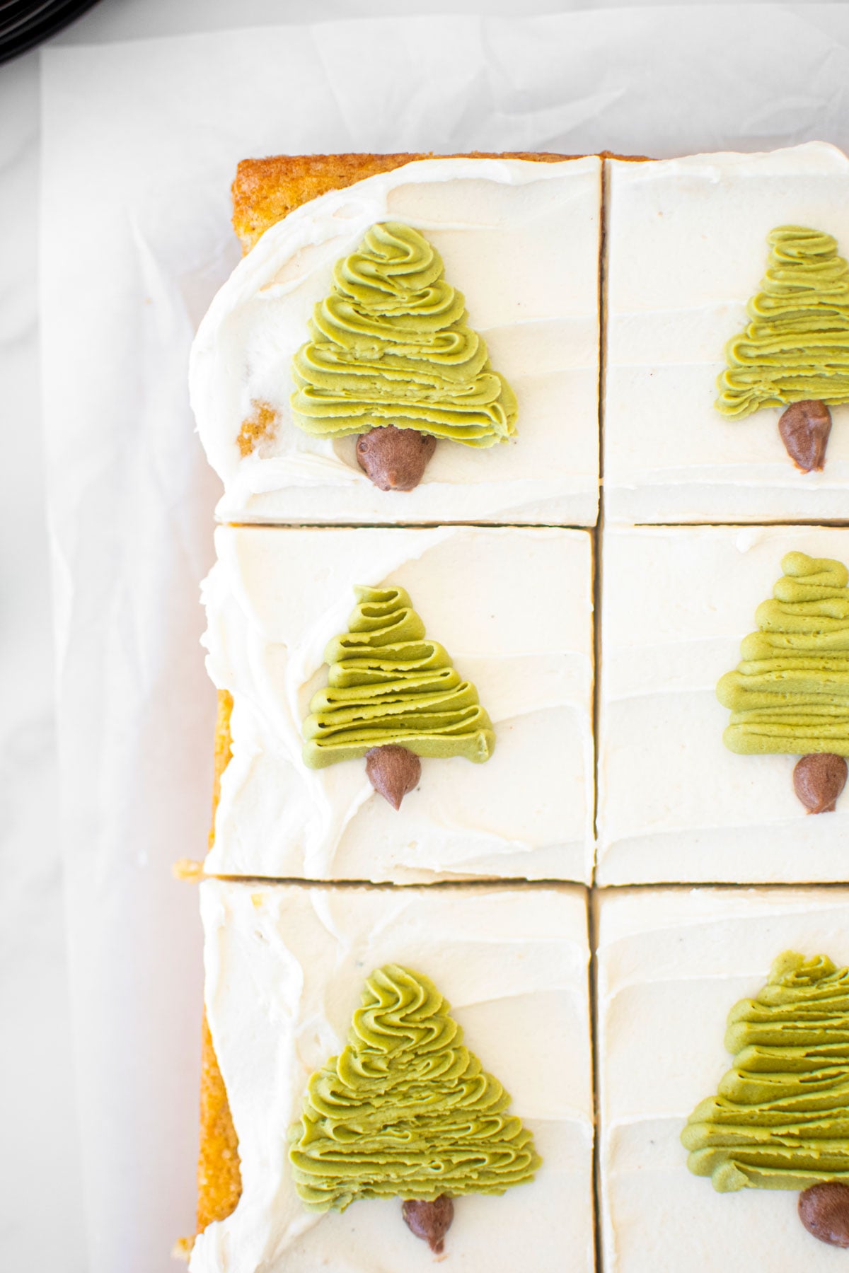 eggnog sheet cake with buttercream christmas trees piped onto each slice on a white parchment paper sheet.