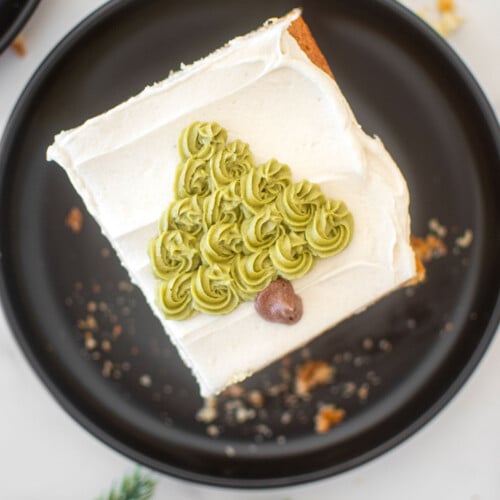 eggnog cake slice with a buttercream christmas tree on it on a black plate on a marble counter.