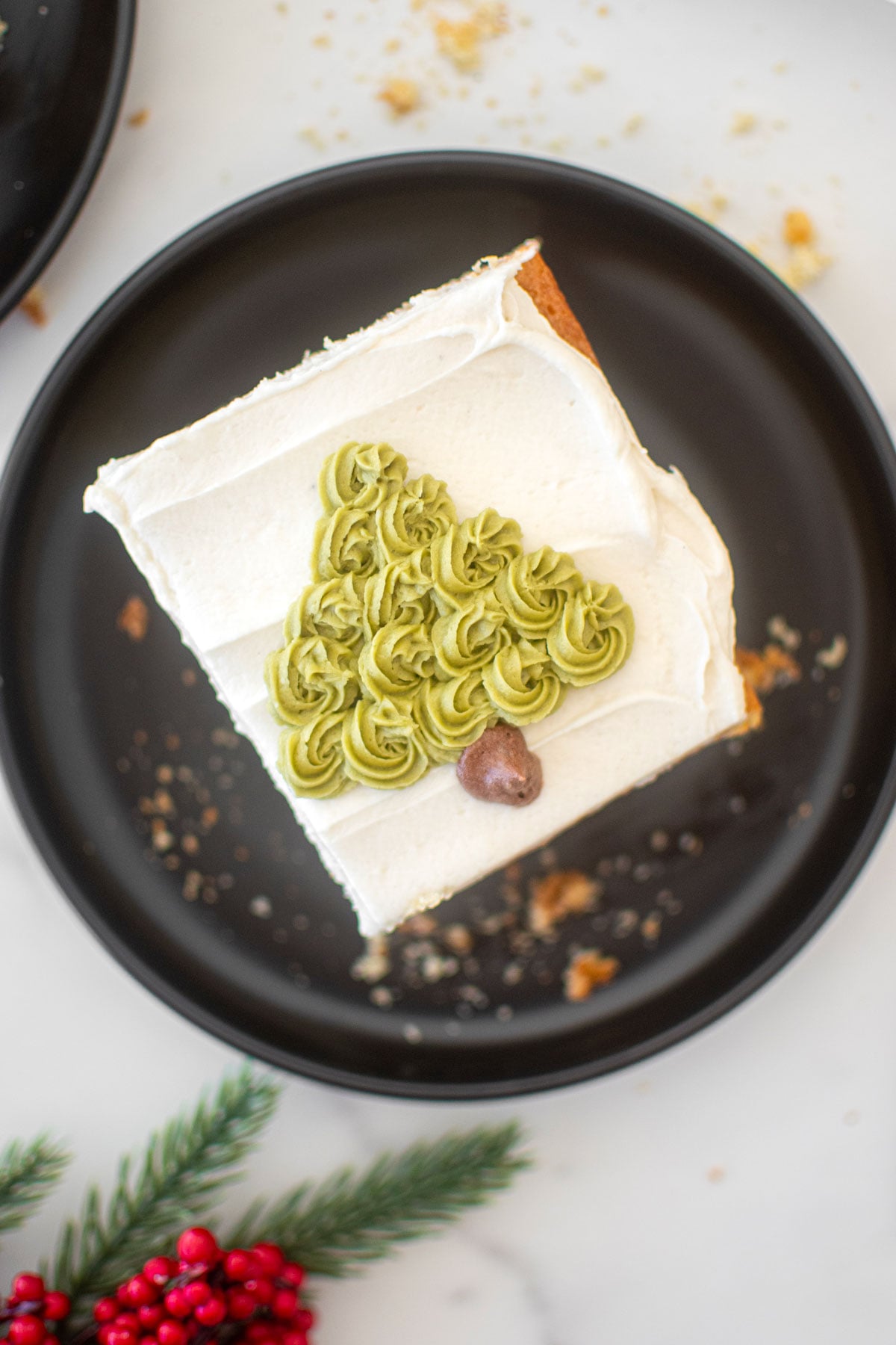 eggnog cake slice with a buttercream christmas tree on it on a black plate on a marble counter.