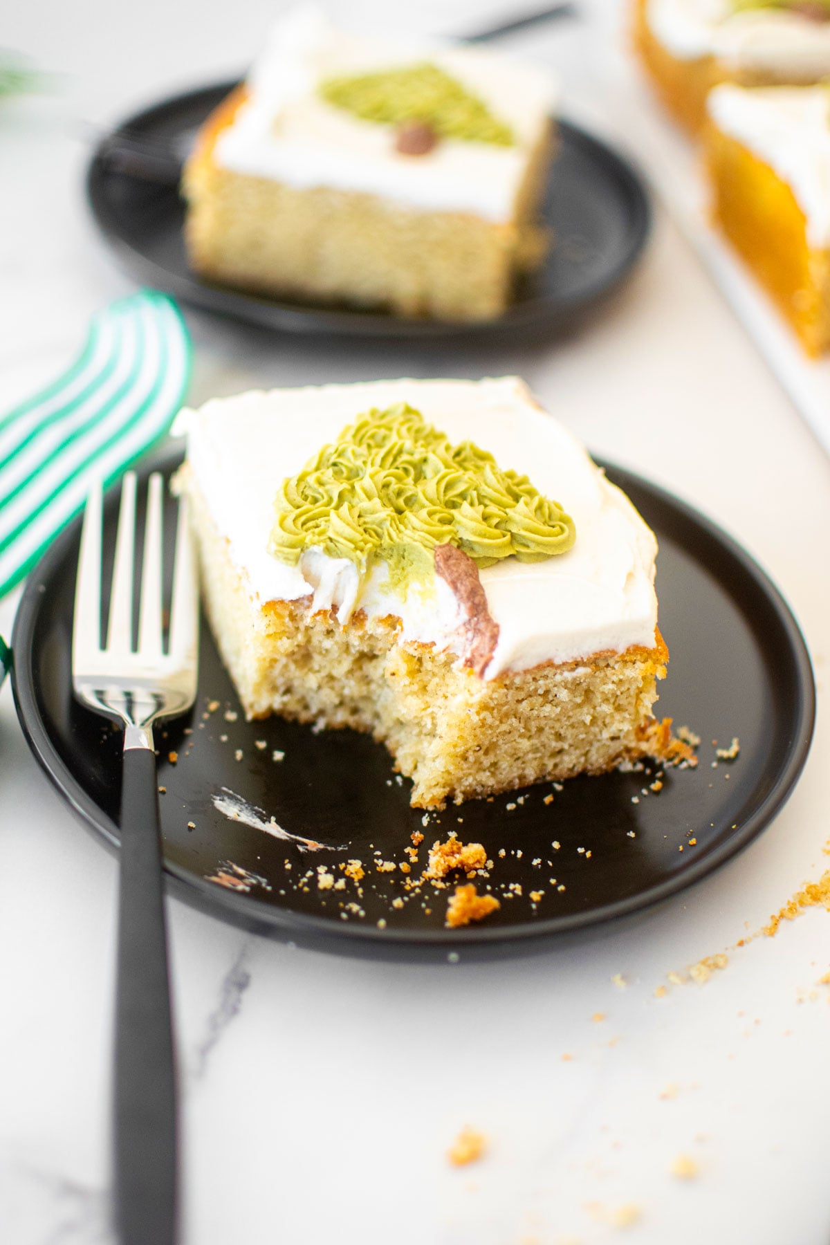 slice of eggnog sheet cake with a buttercream christmas tree on a black cake plate on a marble counter.