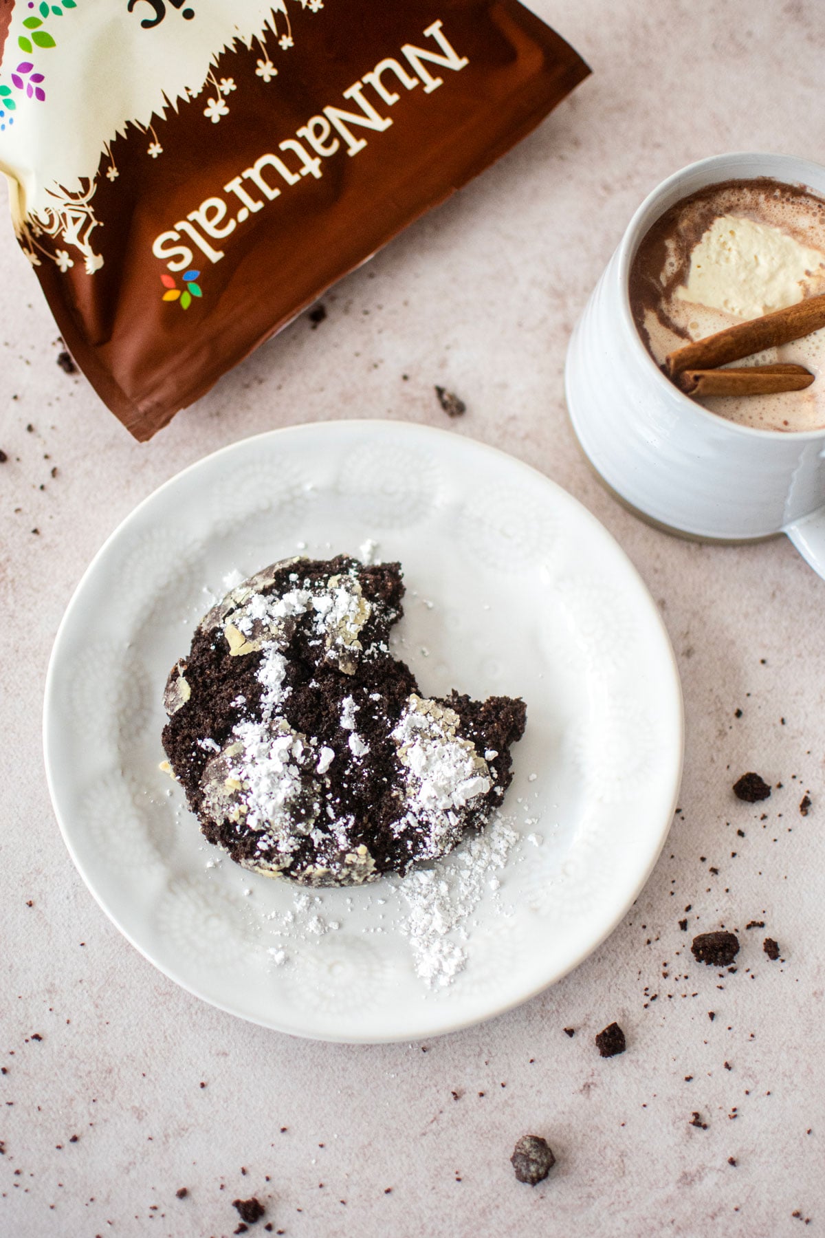 mexican hot chocolate crinkle cookie with a bite taken out on a small plate with a hot cocoa.