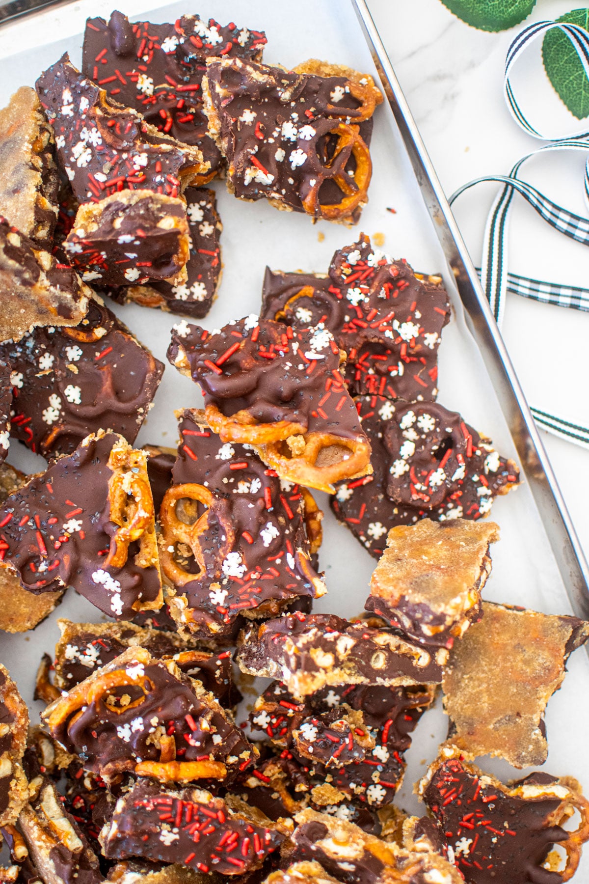 peanut butter pretzel christmas crack on a baking sheet on a marble counter with holiday ribbon.
