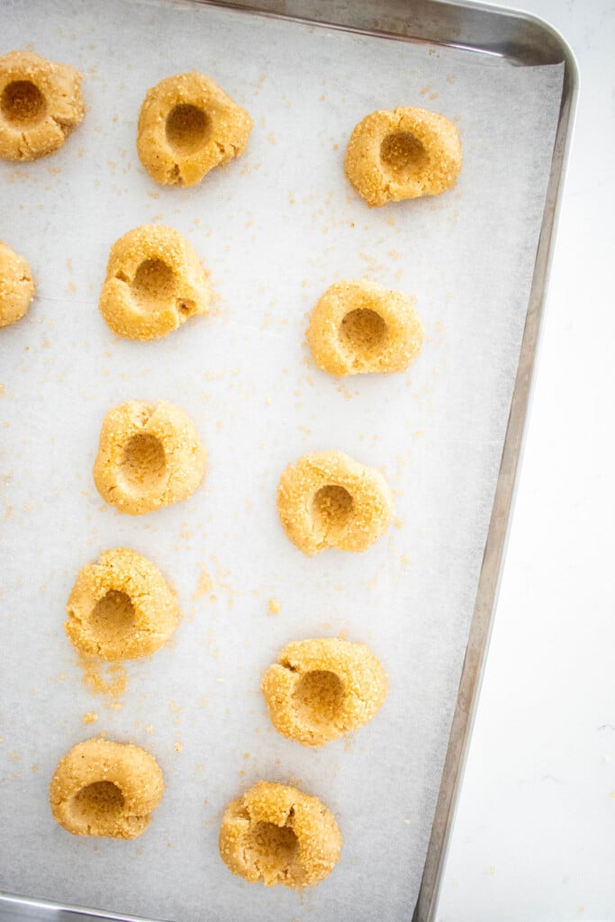 sourdough jam thumbprint cookie dough with holes pressed into dough on a baking sheet on a marble counter.